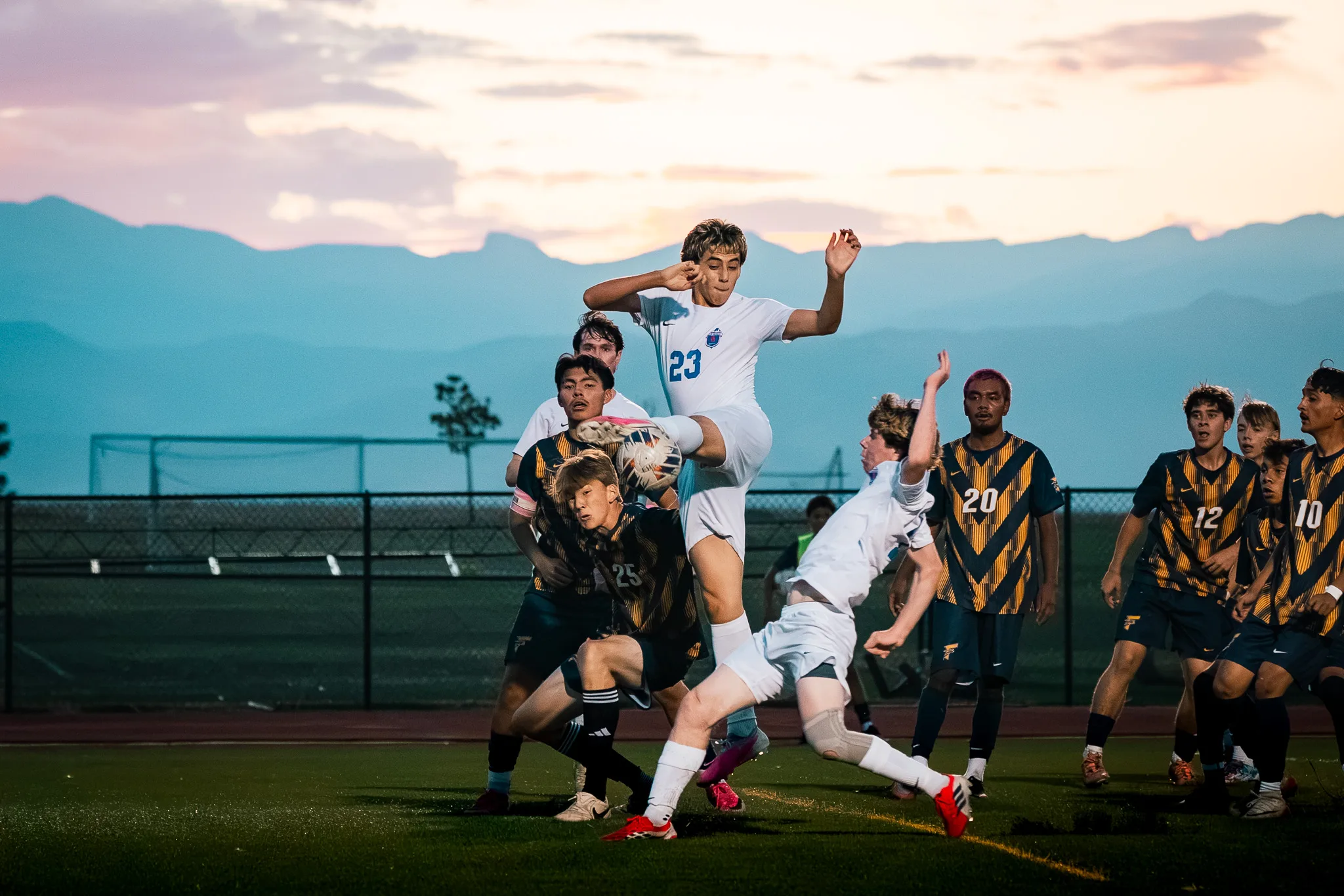 Against the mountains at dusk, Centaurus number 23 leaps with a leg swung up at the ball as Frederick numbers 25, 20, 12 and 10 crowd in